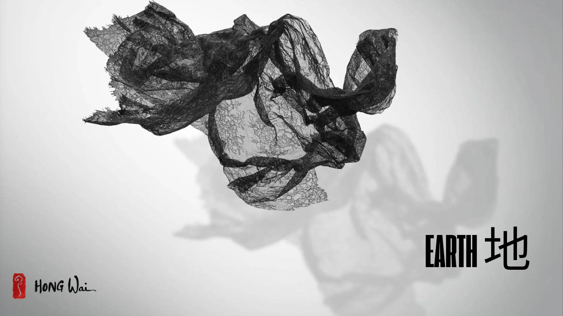 A solitary figure sits on a bench, gazing upward at floating black net-like sculptures against a stark white wall.