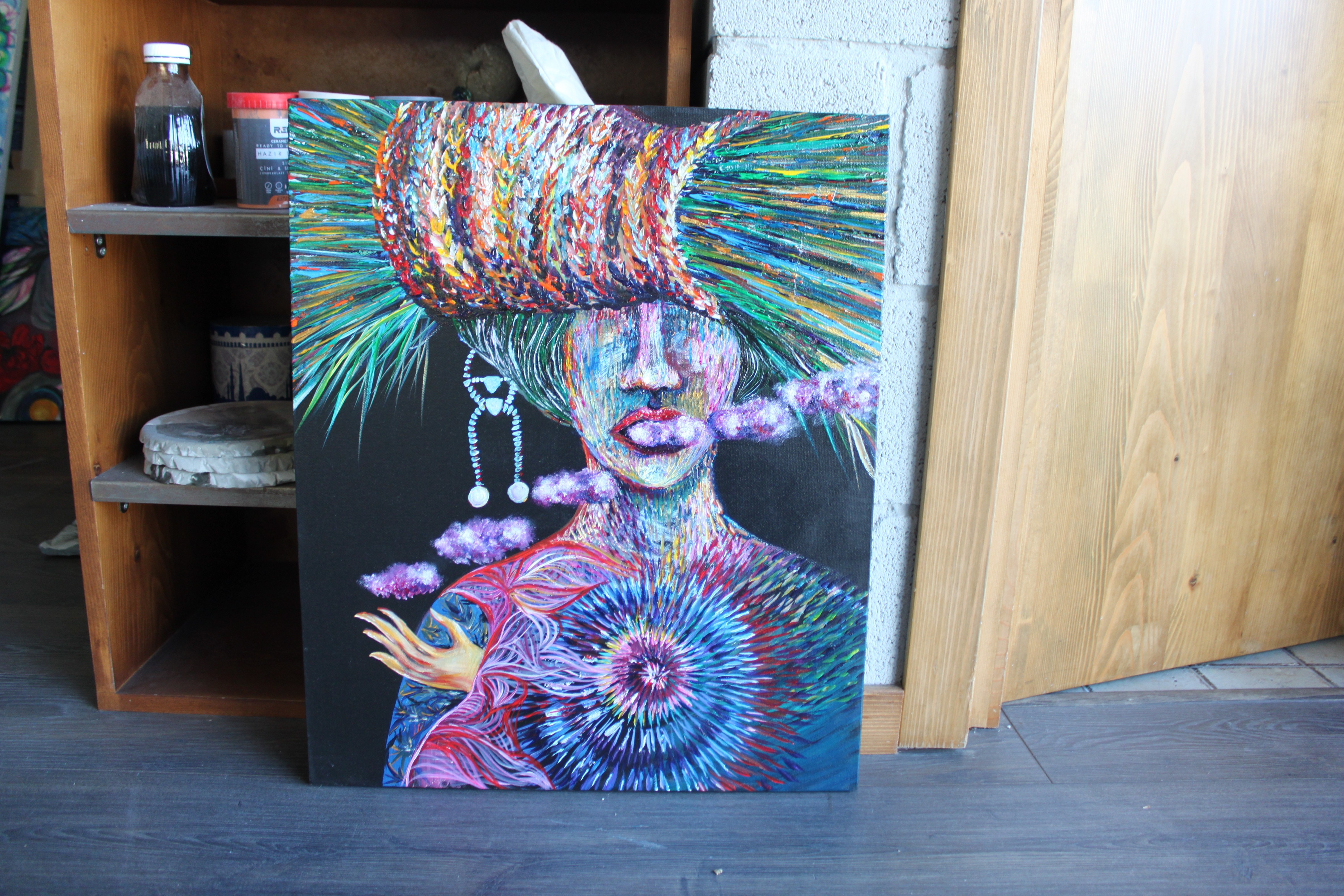 A painting of a woman with a colorful hat on a wall.