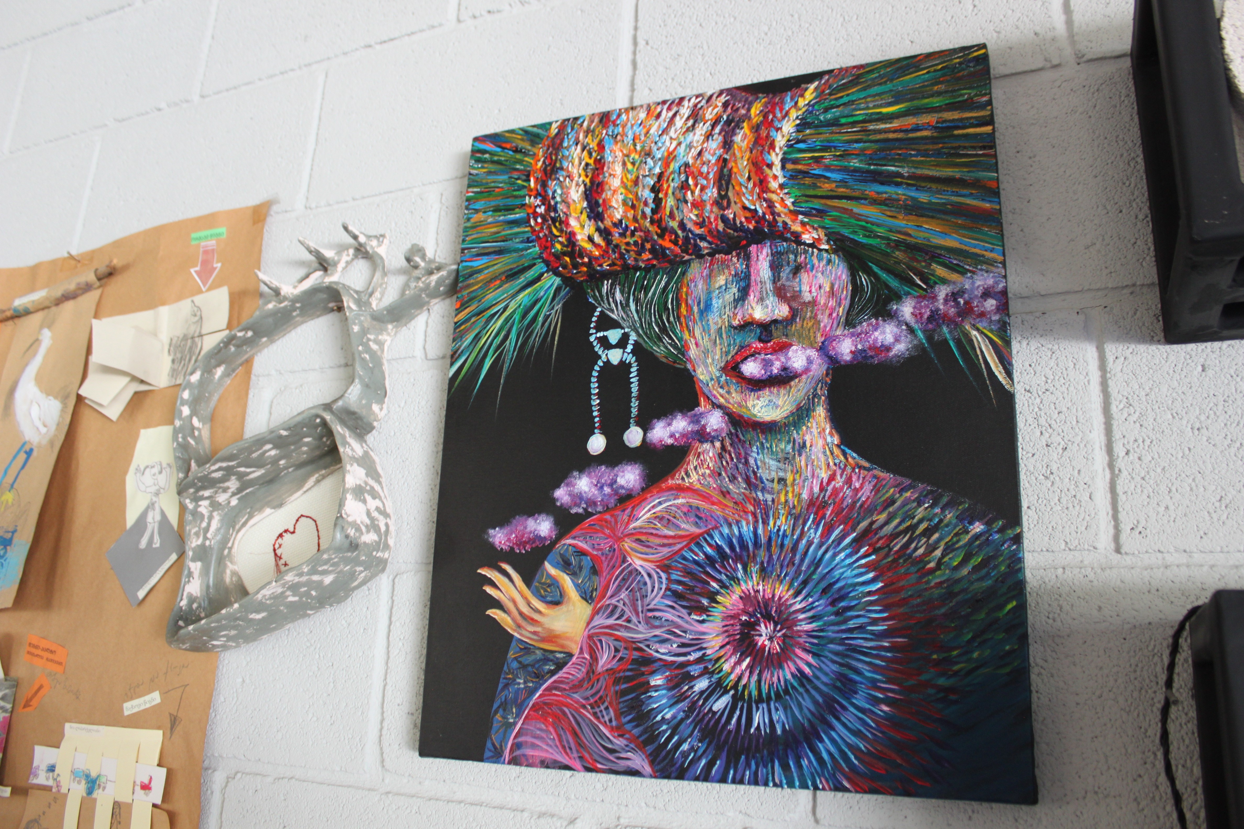 A painting of a woman with a colorful hat on a wall.