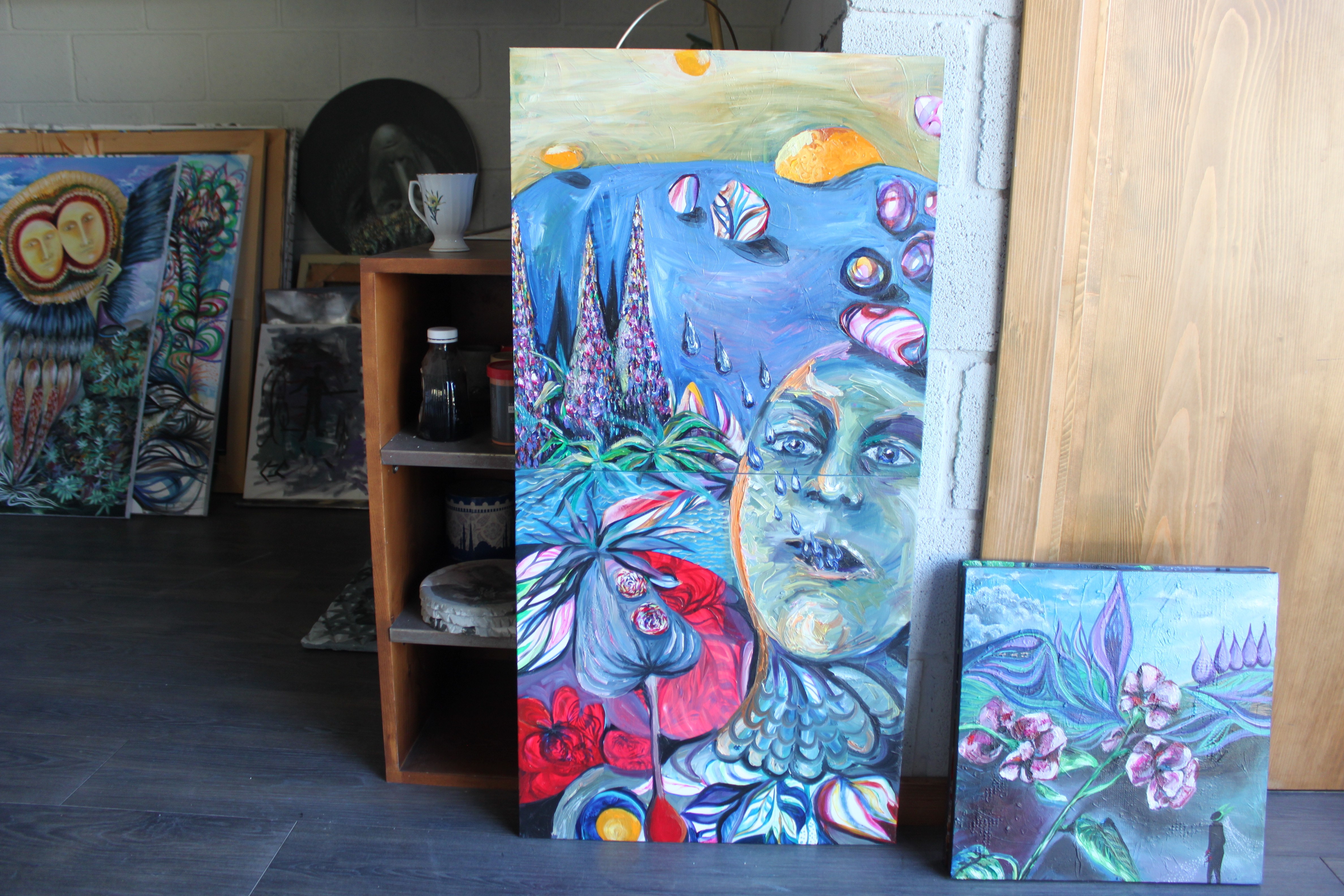 A painting of a woman's face on a wall next to other paintings.