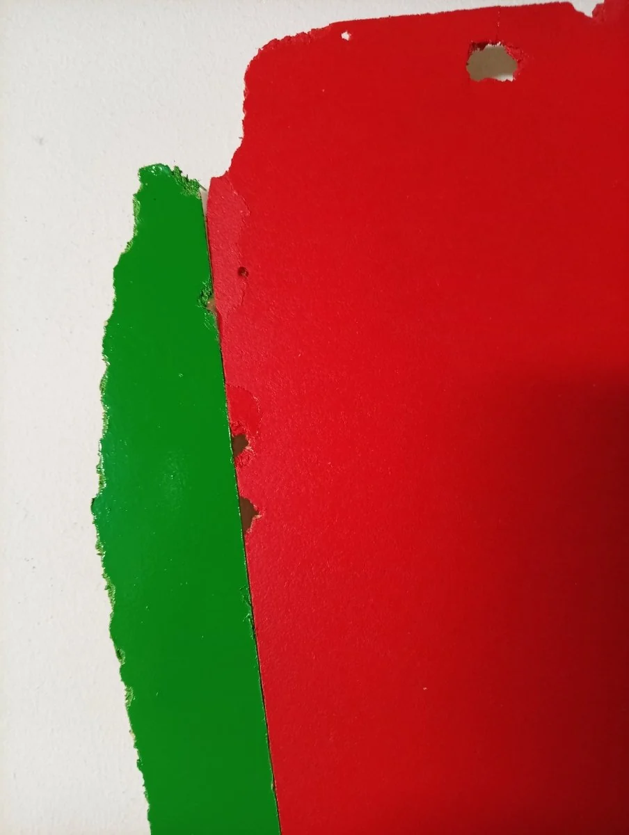 A bold, abstract composition featuring a red shape with a green vertical strip and a hole at the top.