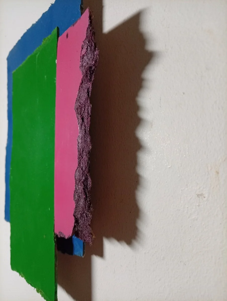 A layered composition of three rectangular paper sheets in blue, green, and pink against a white background.