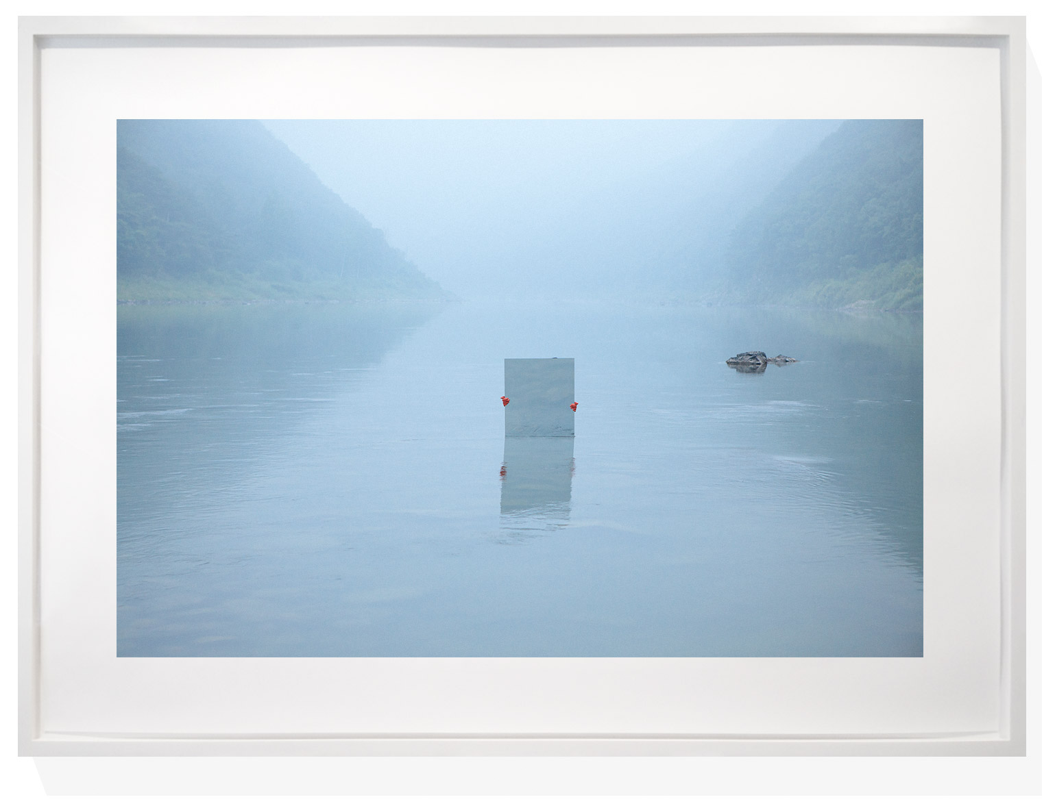 A minimalist framed photograph of a foggy river with a reflective rectangular object floating in the center.