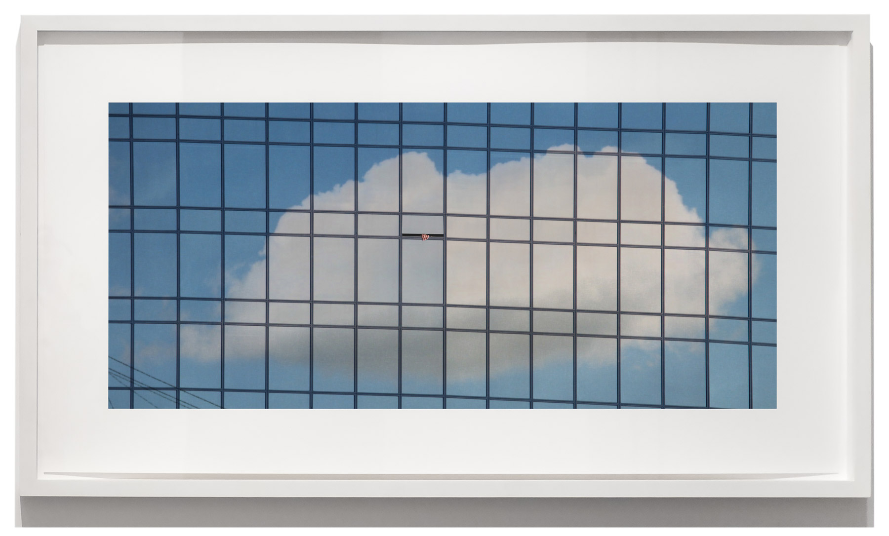 A framed photograph of a cloud reflected in the grid-like glass facade of a modern building.