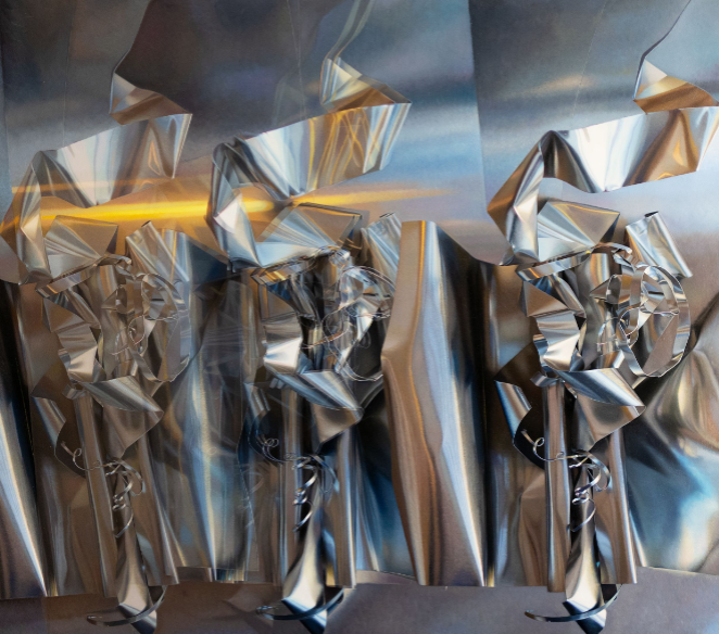 A metallic sculpture featuring three abstract, ribbon-like figures against a reflective background.