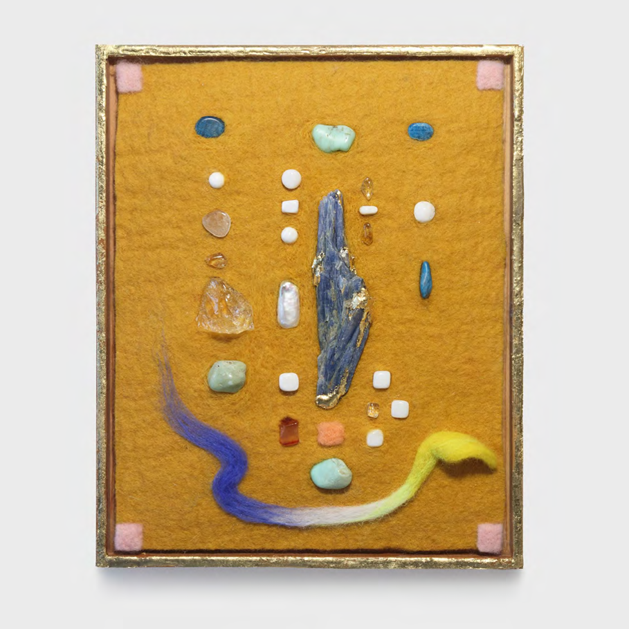 A mixed-media collage featuring a central blue crystal surrounded by scattered stones and colorful fibers on a golden felt background.