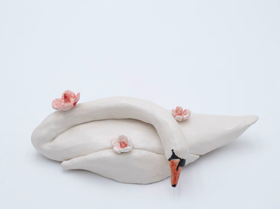 A white ceramic swan sculpture with small pink flowers resting on its body.