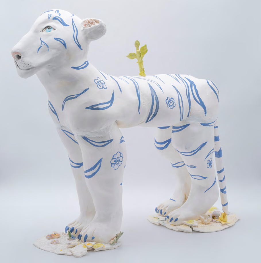 A white ceramic sculpture of a tiger-like figure with blue stripes and floral motifs, standing on a cracked base.