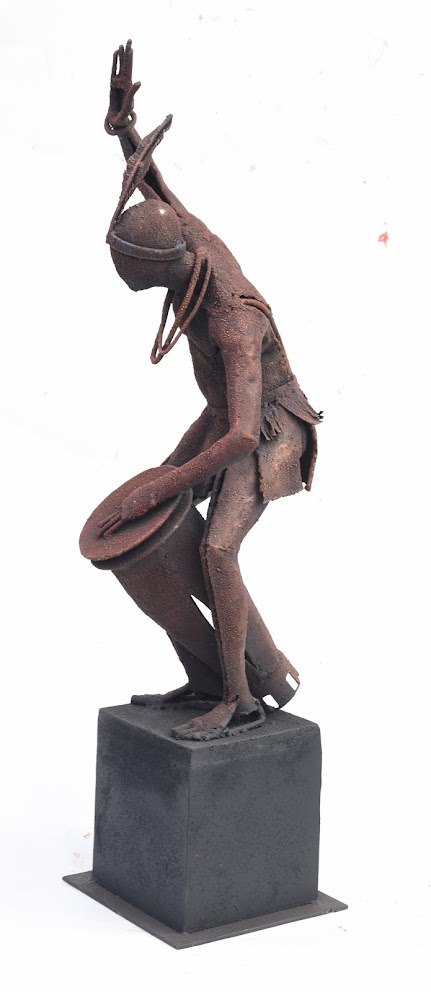 A rusted metal sculpture of a figure in motion, captured mid-dance on a dark pedestal.
