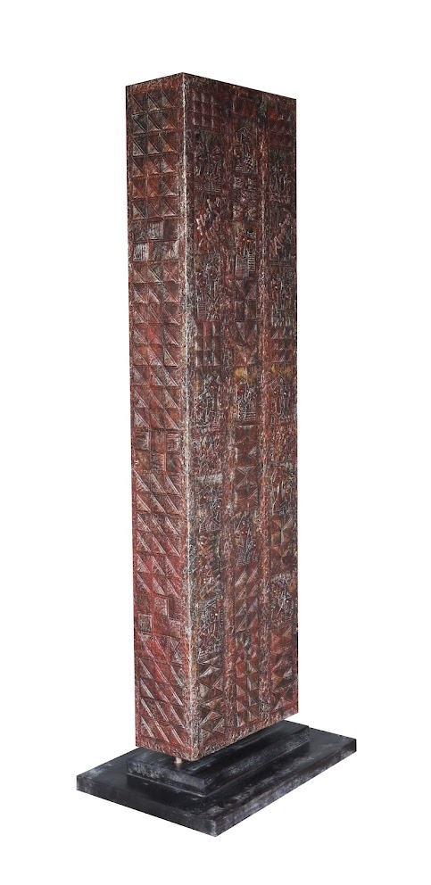 A tall, rectangular sculpture with intricate geometric carvings and a dark base.