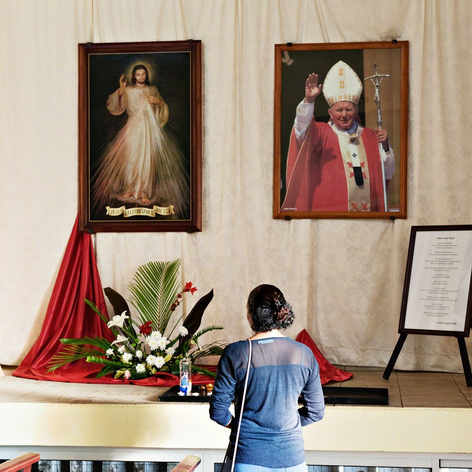 A woman standing in front of a painting of Jesus and a picture of a priest.