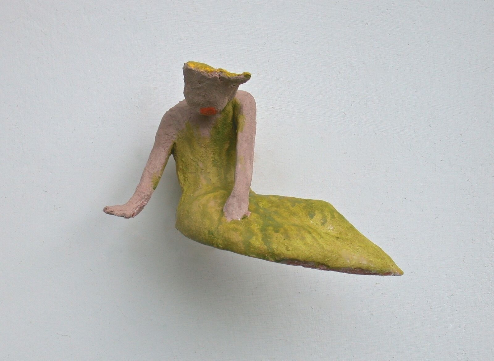 A small, abstract sculpture of a seated figure with a blocky head and flowing green lower body.