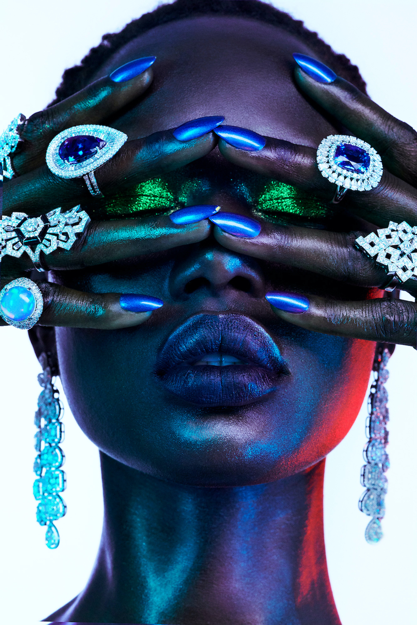 A woman with blue and green nails covering her eyes with her hands.