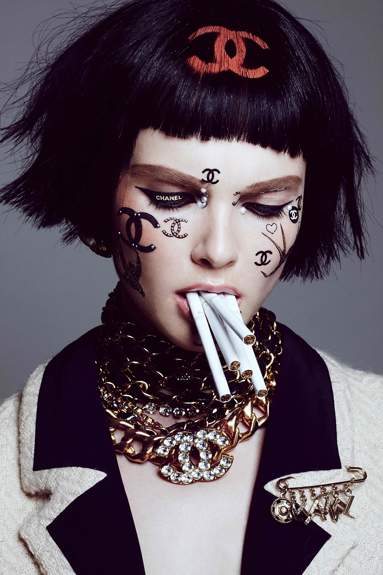 A woman with black hair and a chanel necklace smoking a cigarette.