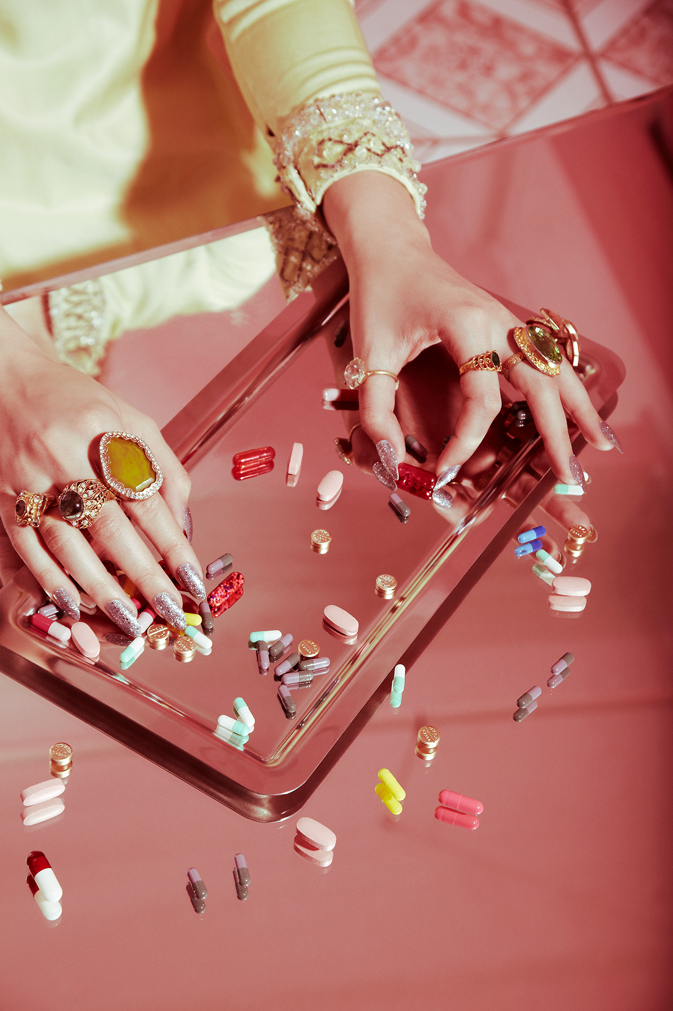 A woman's hands on a pink table with pills scattered around her.