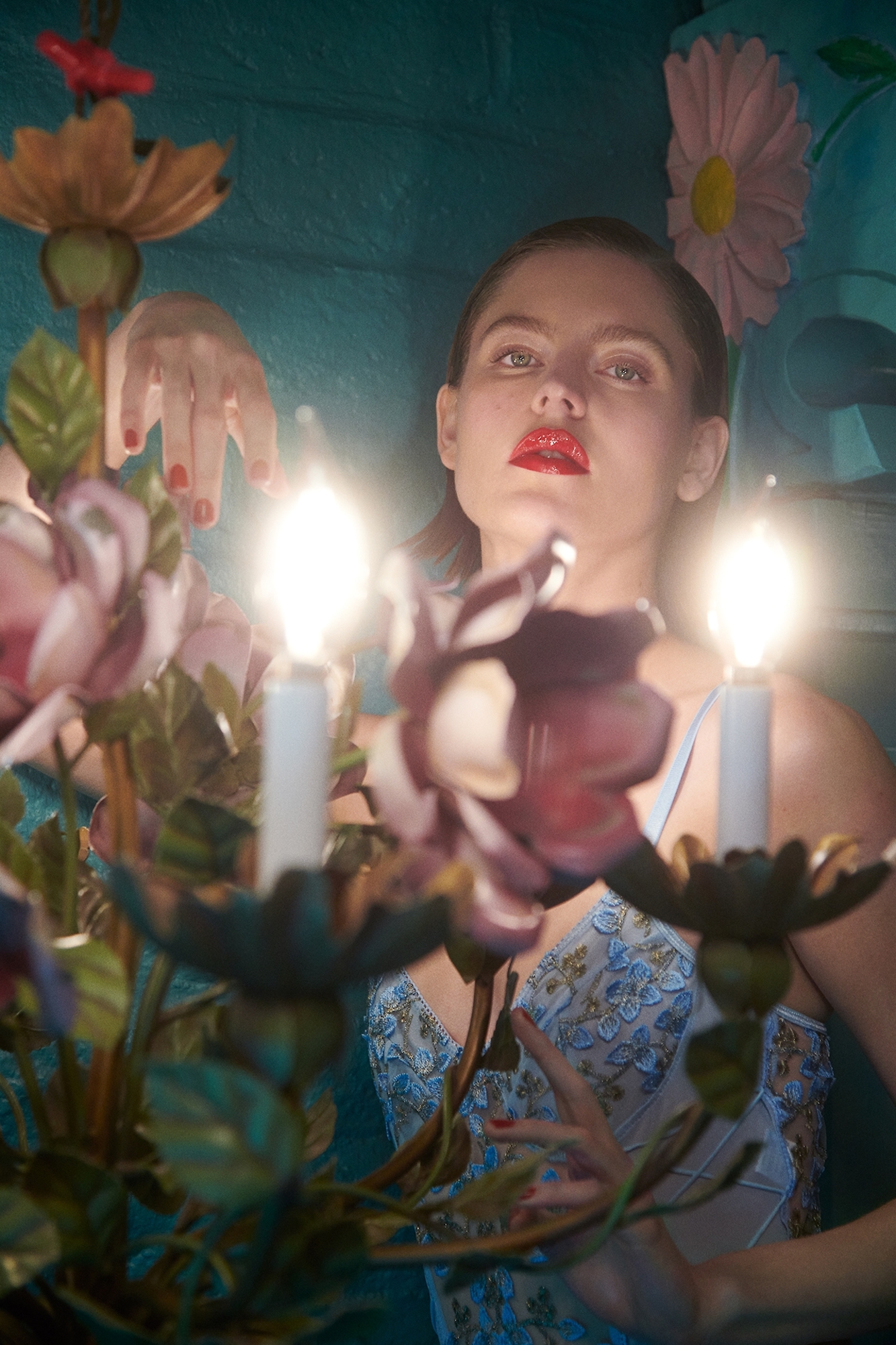 A woman in a blue dress holding a candle in front of flowers.