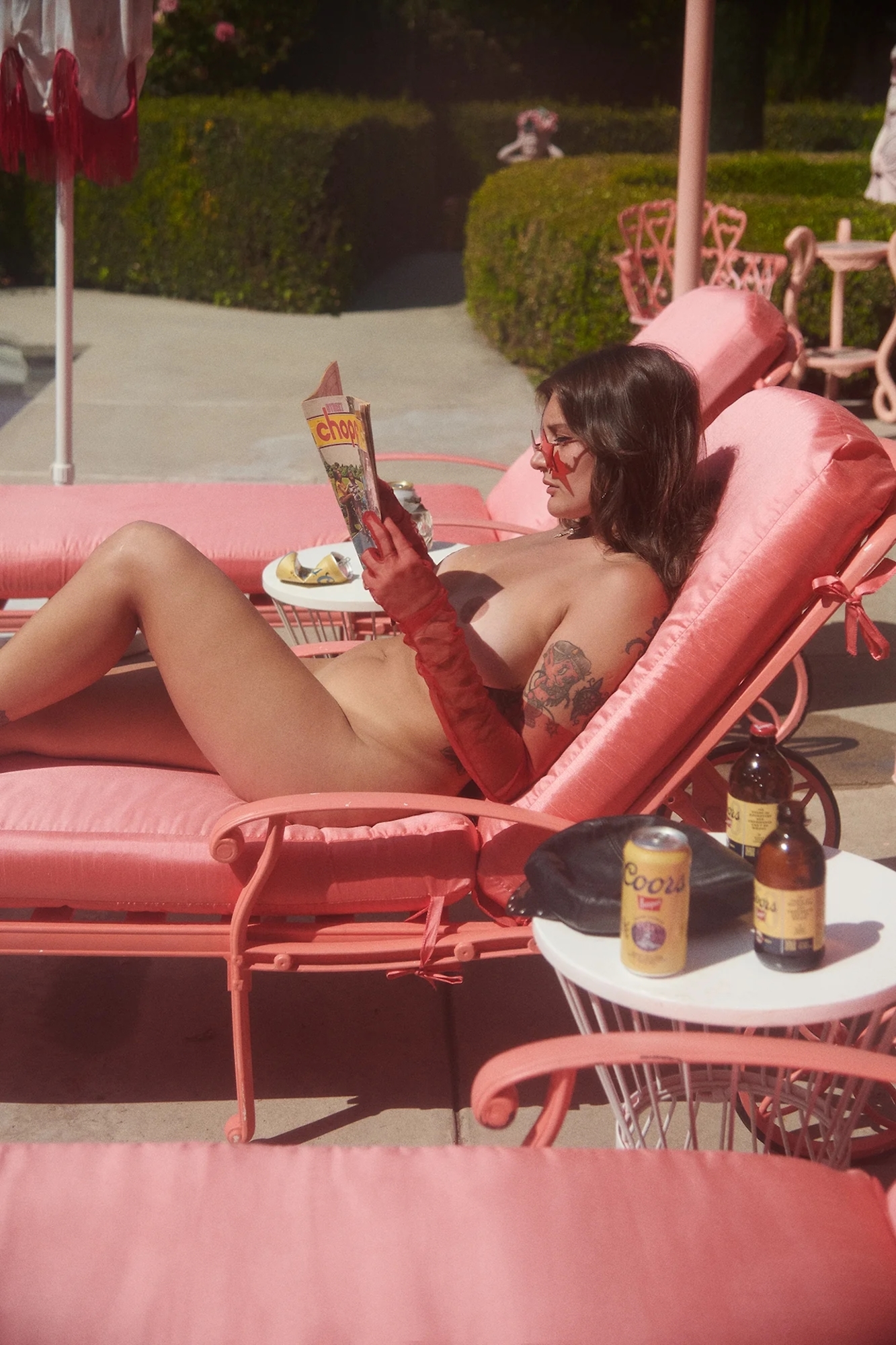 A woman laying on a pink lounge chair reading a magazine.