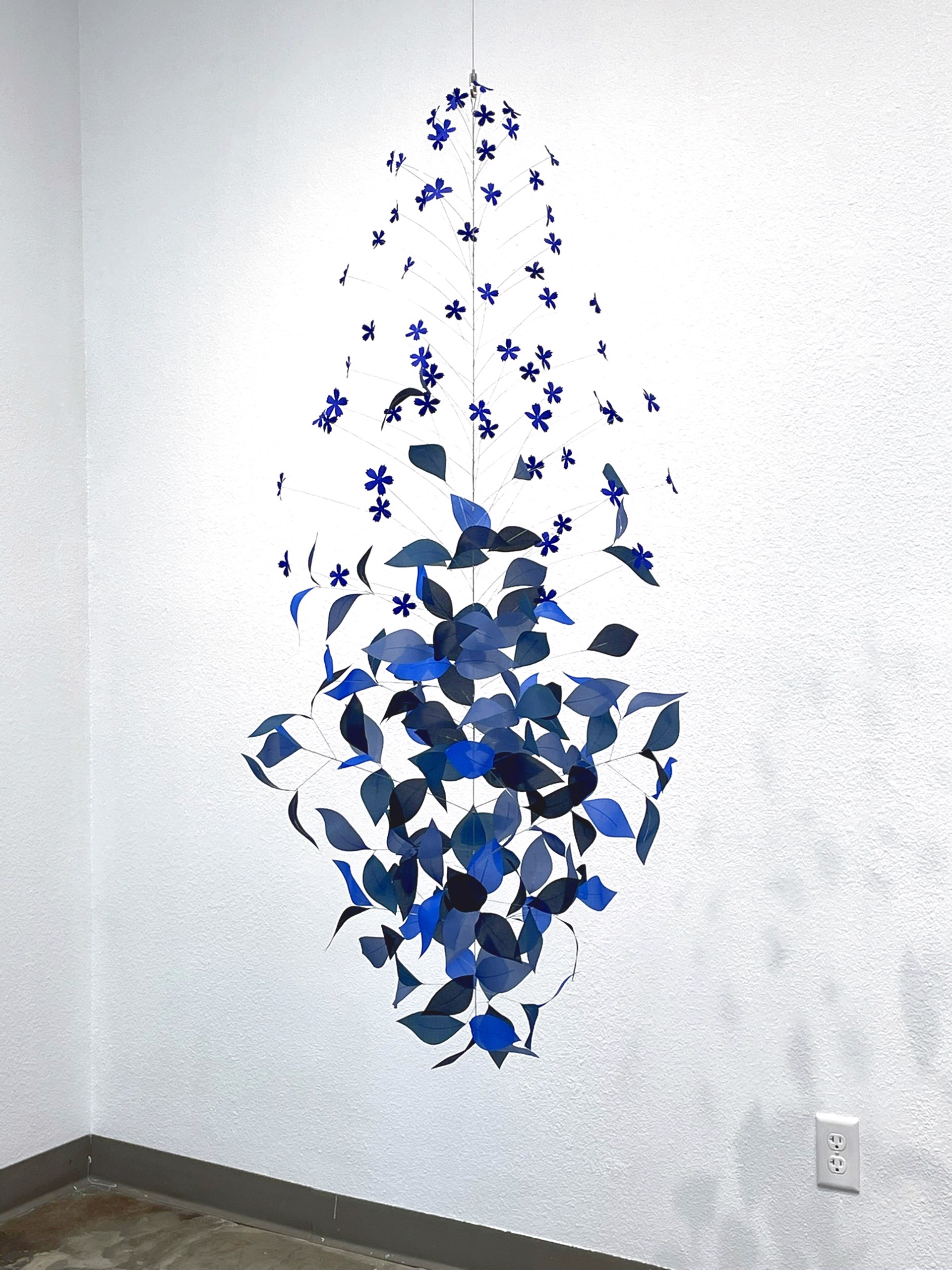 A vertical mobile sculpture featuring cascading blue leaves and star-shaped cutouts against a stark white background.