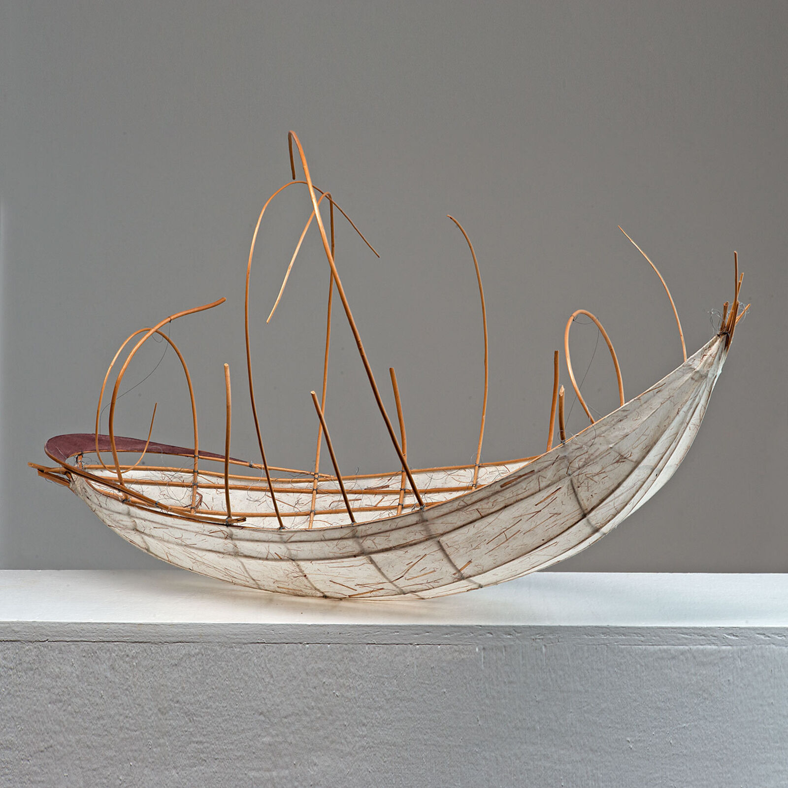 A sculptural vessel with a curved white base and an intricate framework of thin, brown, flexible rods.