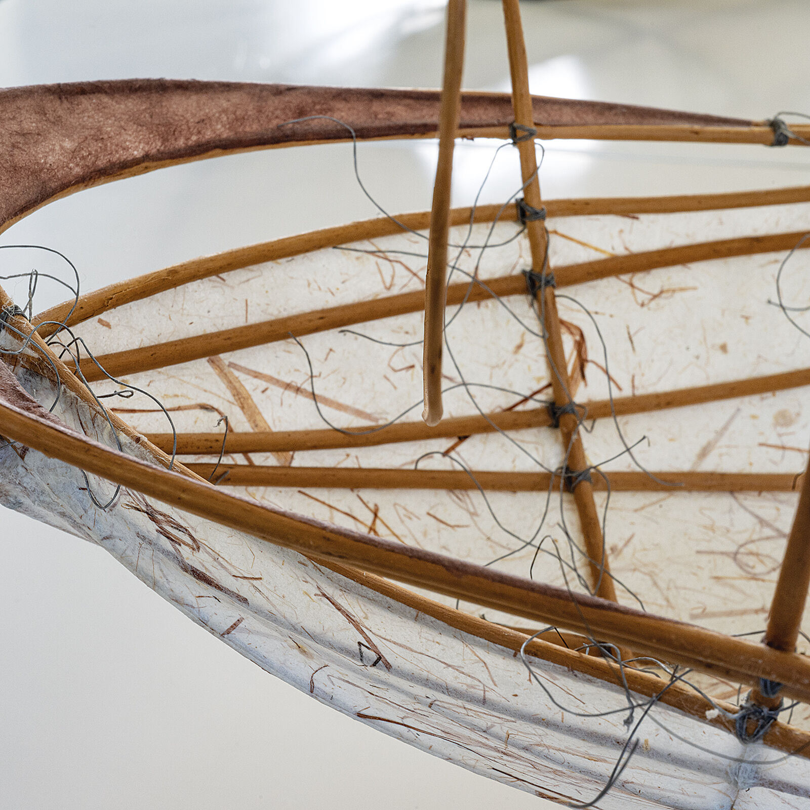 A sculptural vessel with a curved white base and an intricate framework of thin, brown, flexible rods.