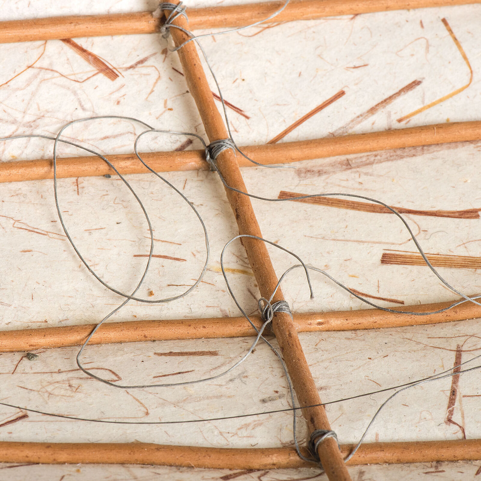 A sculptural vessel with a curved white base and an intricate framework of thin, brown, flexible rods.
