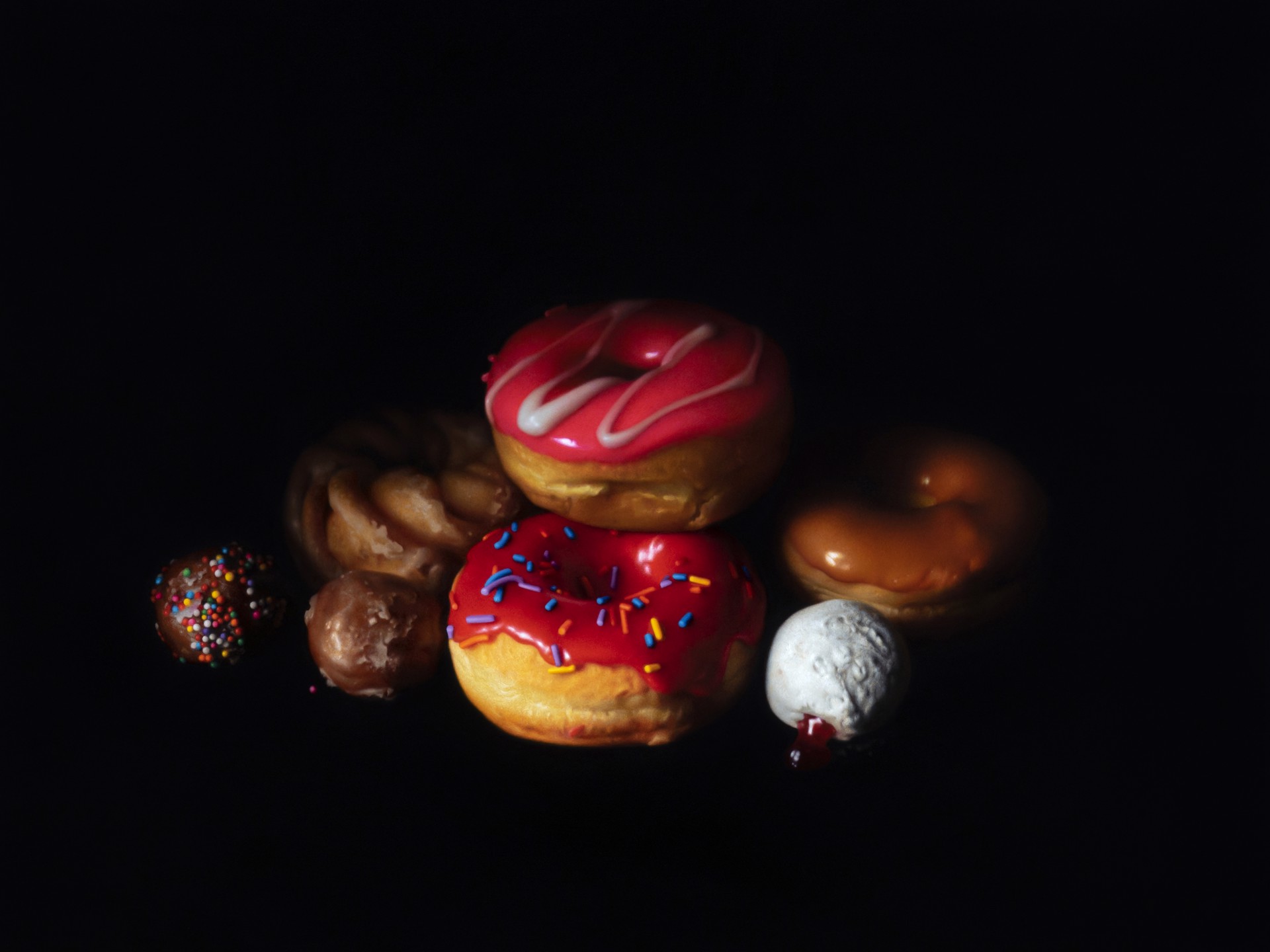 A still life arrangement of colorful donuts and pastries against a dark background.