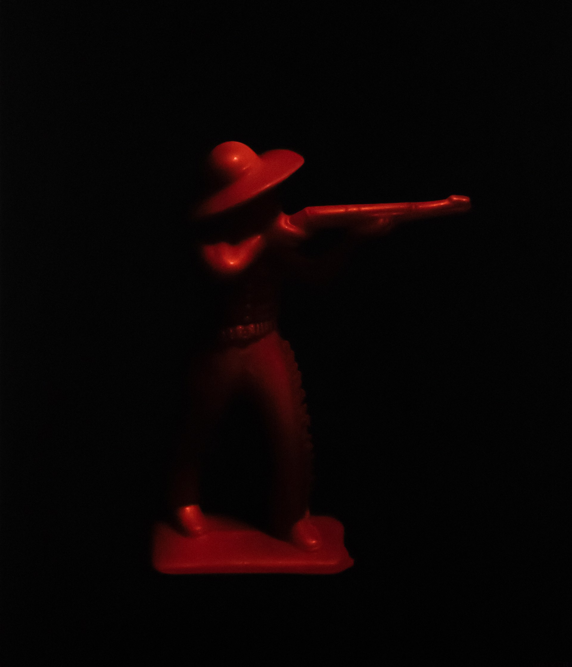 A red figurine of a cowboy holding a gun in the dark.