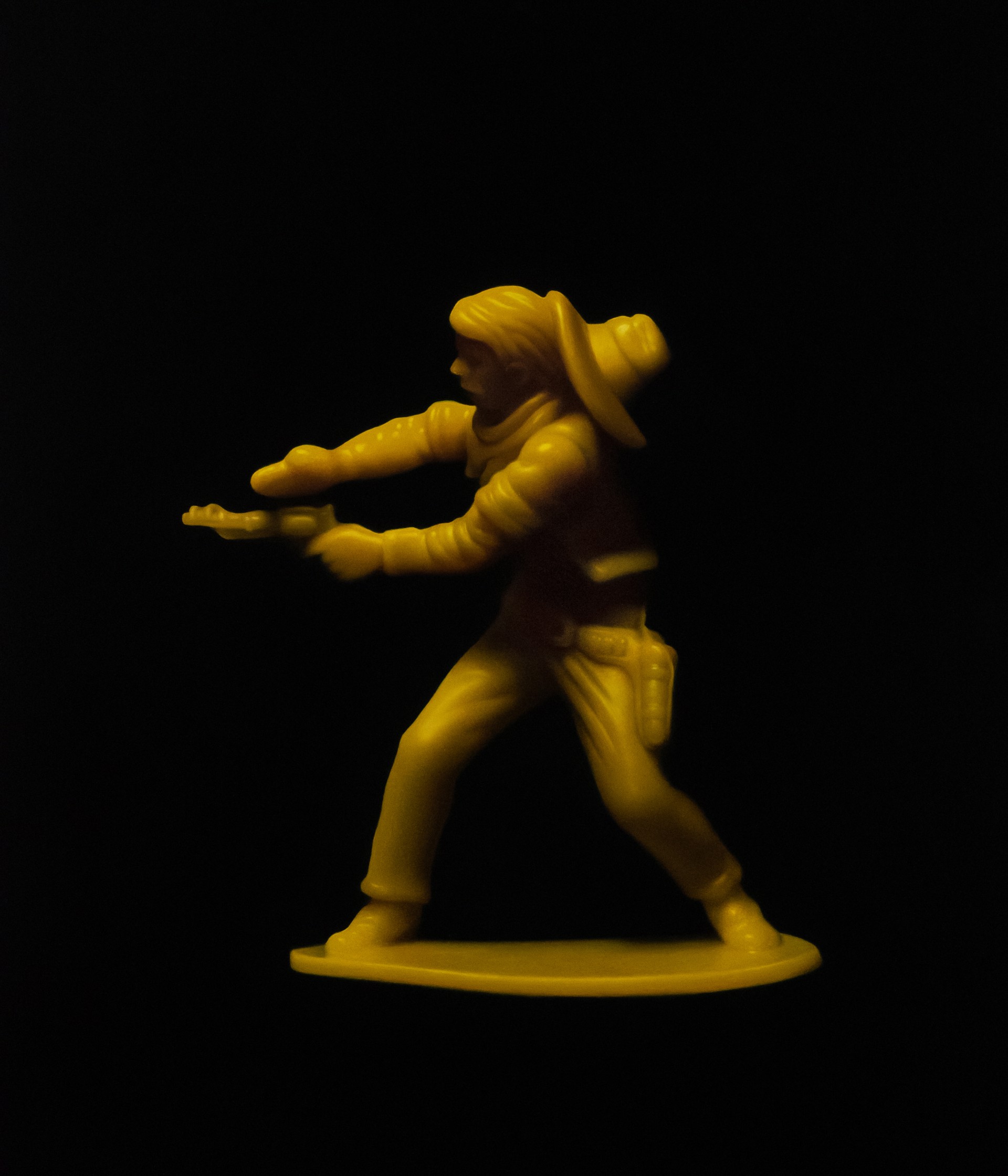 A yellow toy figure of a man holding a gun.