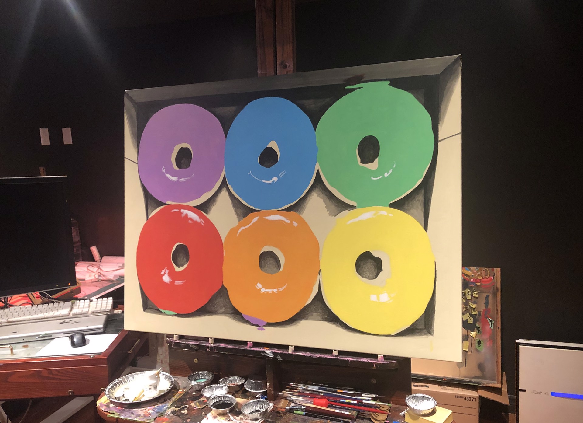 A vibrant display of six colorful glazed donuts arranged in two rows within a cardboard box.