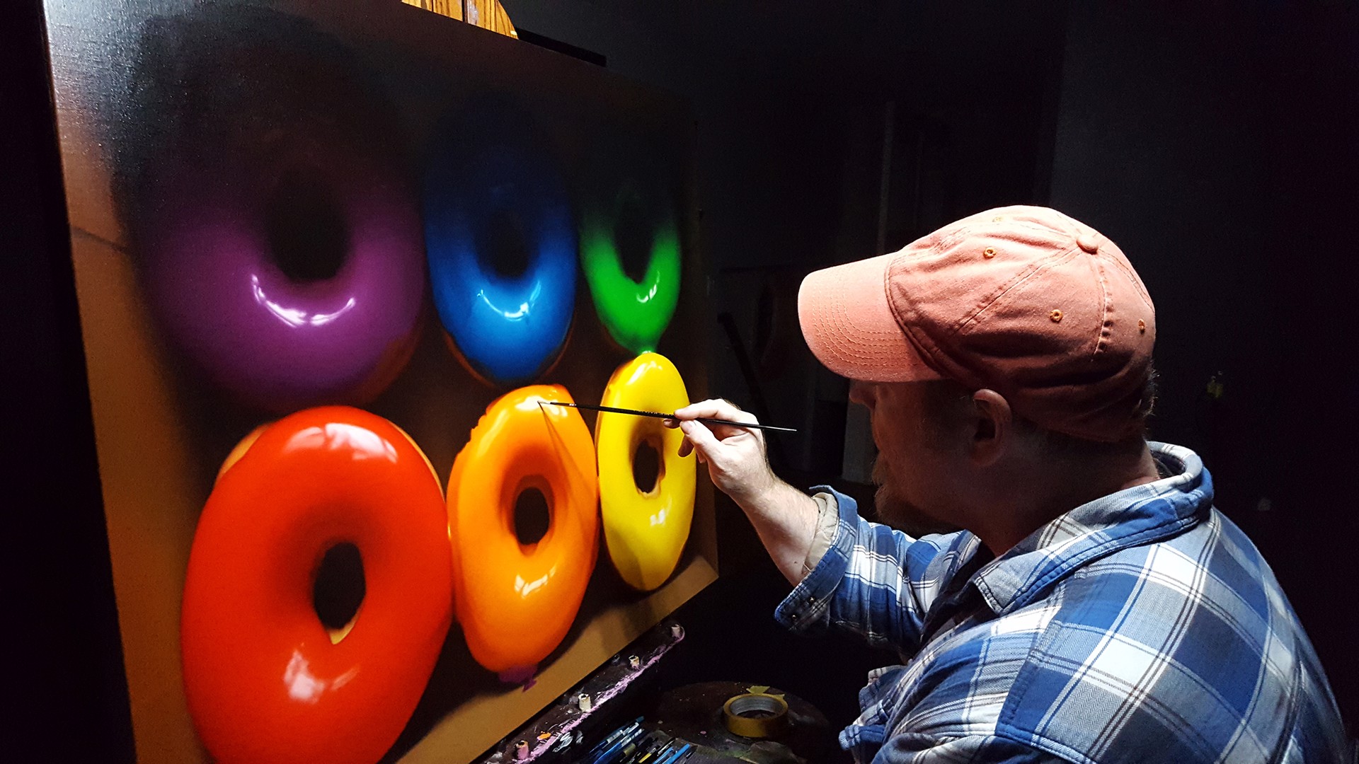 A vibrant display of six colorful glazed donuts arranged in two rows within a cardboard box.