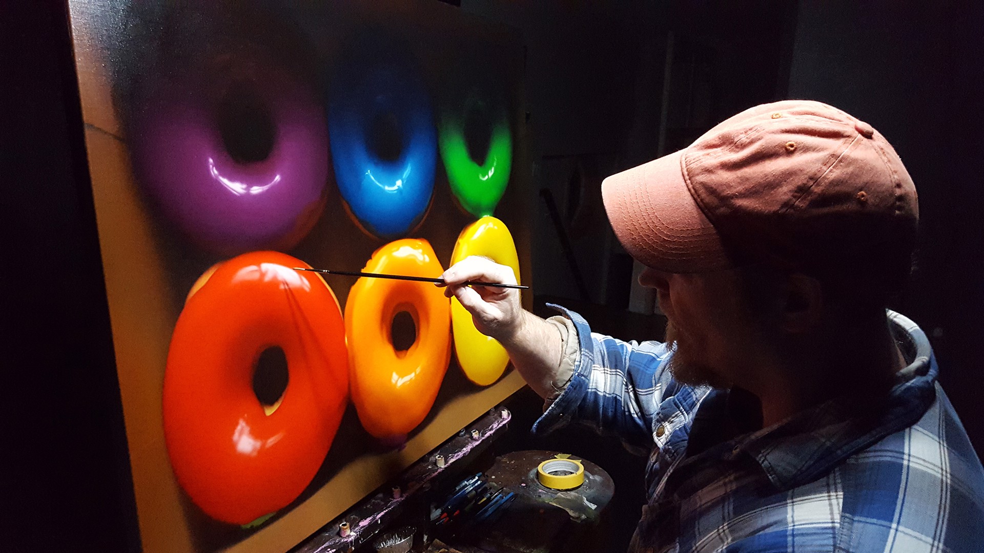 A vibrant display of six colorful glazed donuts arranged in two rows within a cardboard box.