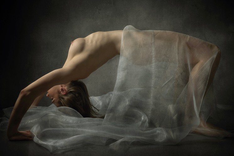A nude woman laying on the ground with a white sheet covering her body.