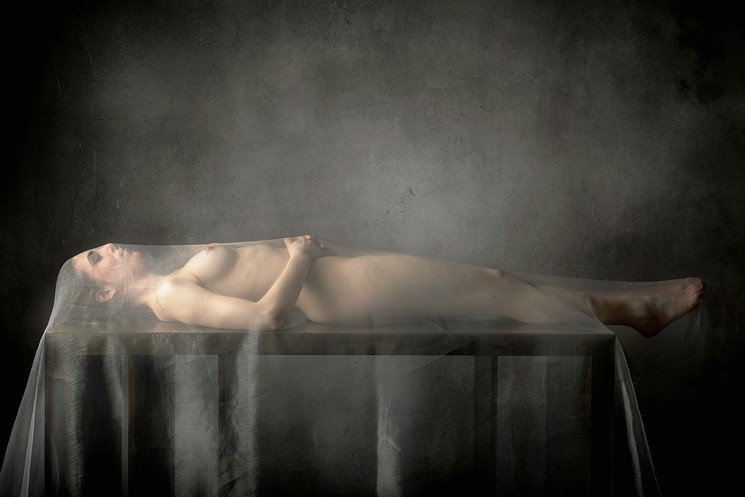 A nude woman laying on a table covered in a veil.