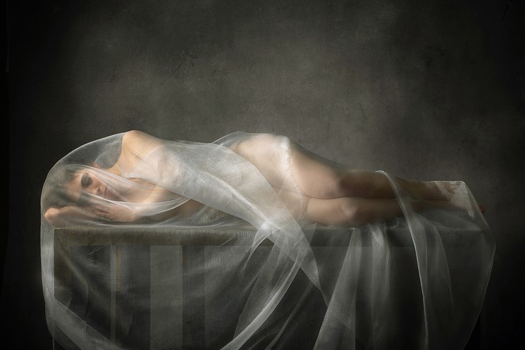 A woman laying on top of a table covered in a veil.