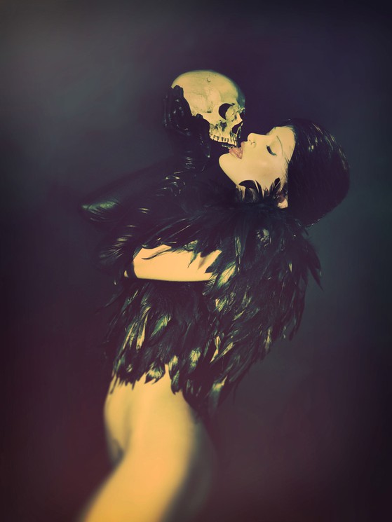 A dramatic portrait of a person in a feathered costume embracing a skull against a dark background.