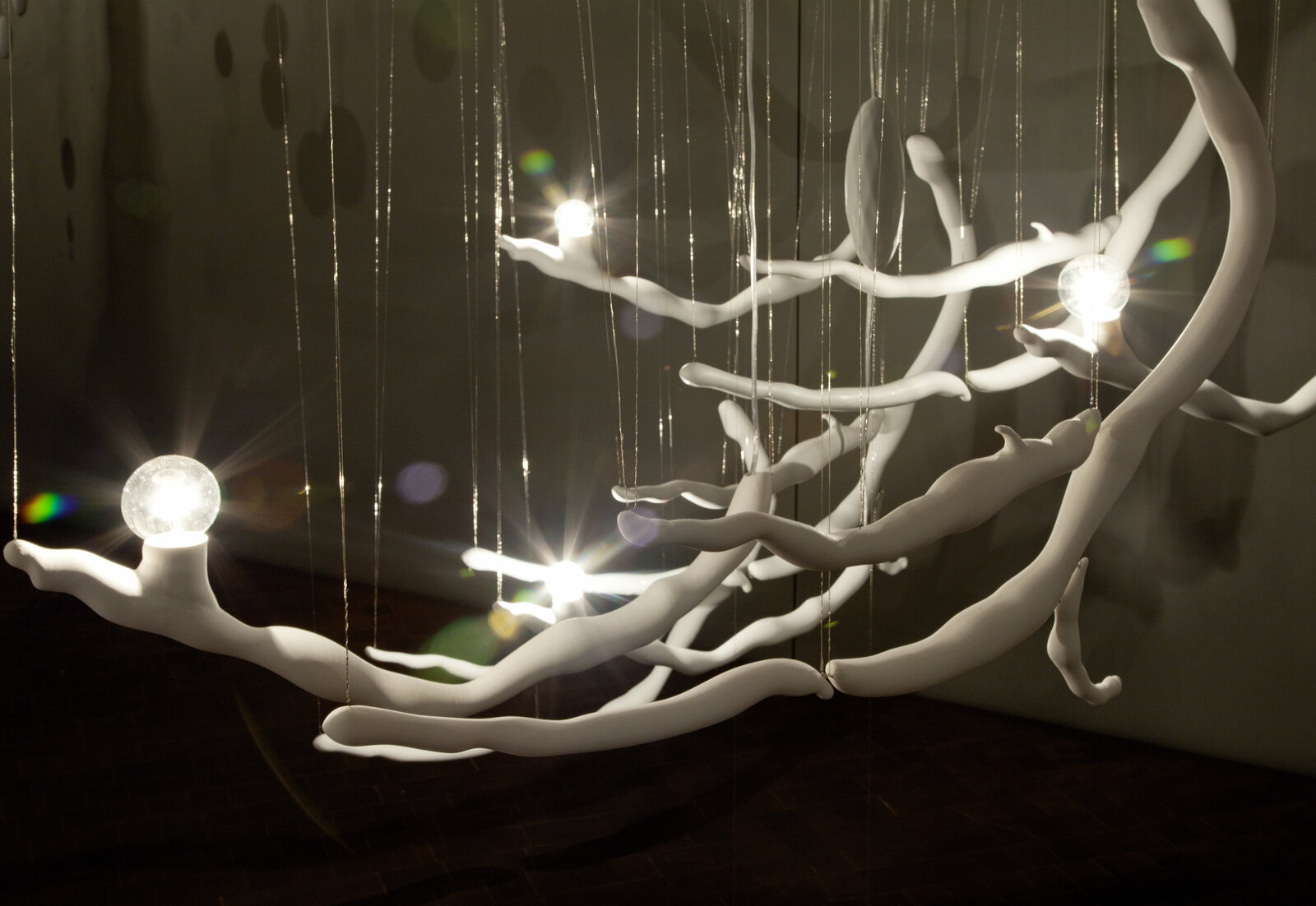 "A suspended installation of white, branch-like structures with glowing lights and floating discs in a monochromatic gallery space."