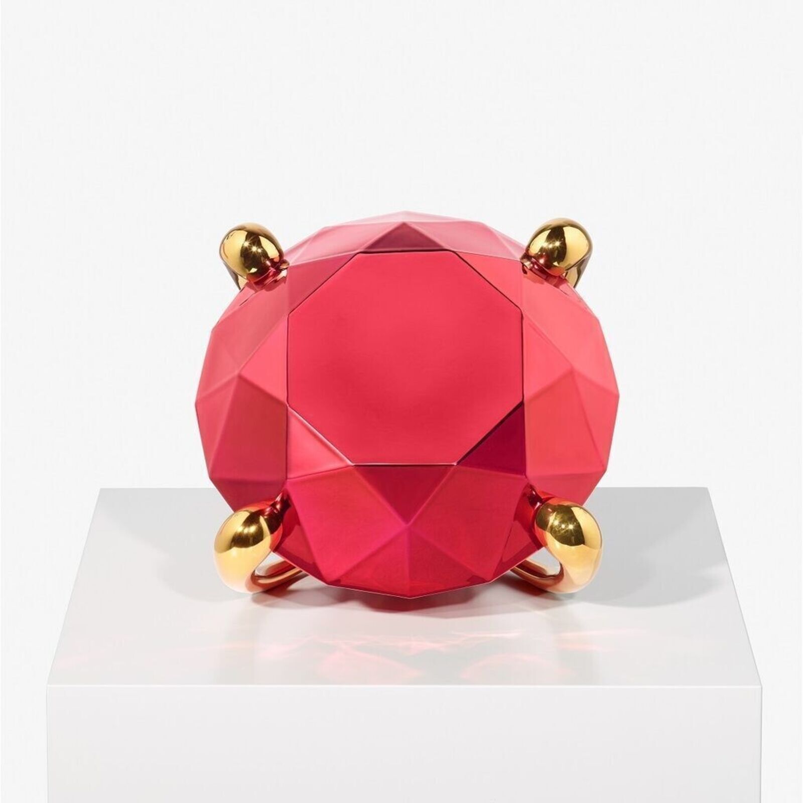 A faceted red sphere with gold accents resting on a white pedestal.