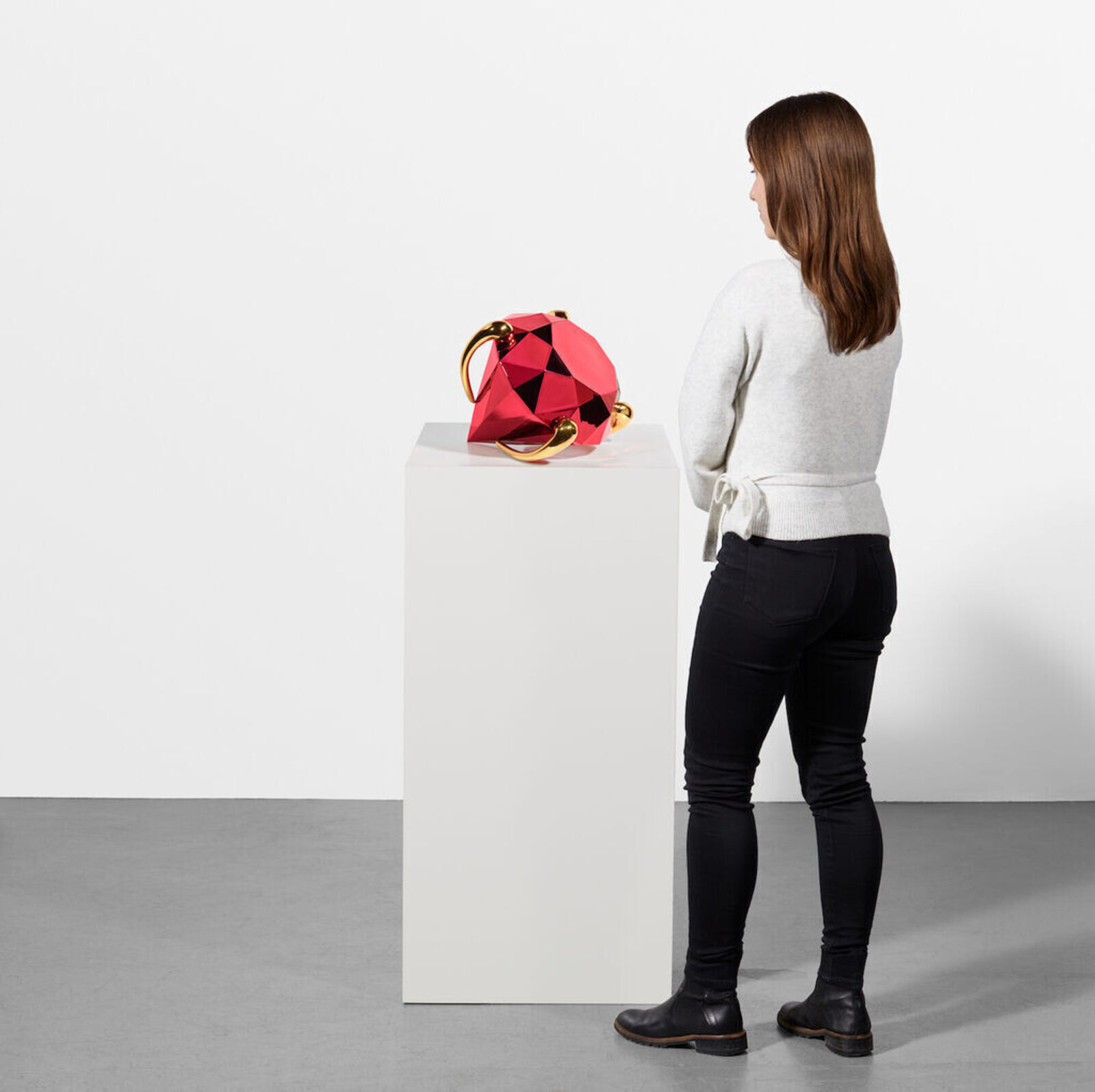 A faceted red sphere with gold accents resting on a white pedestal.