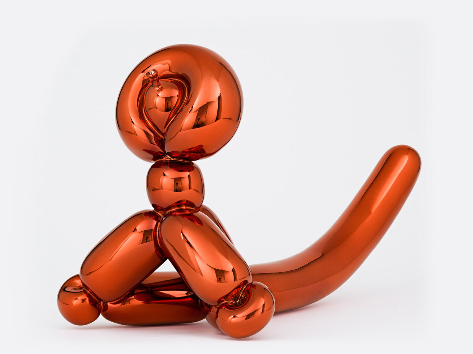 An orange balloon dog sitting on a white surface.