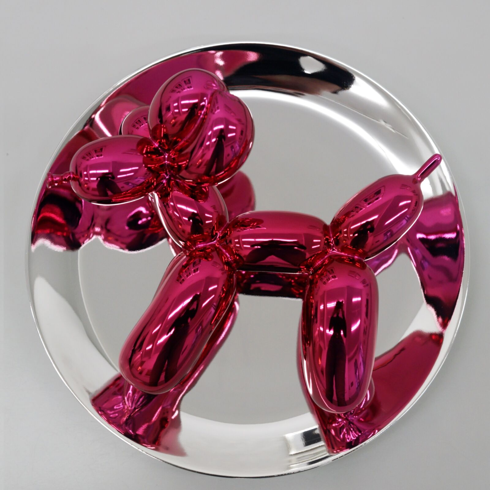 A trio of glossy, metallic balloon-dog sculptures displayed on clear stands against a neutral background.