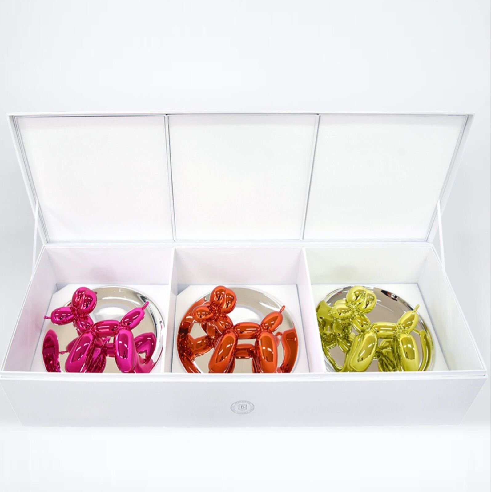 A trio of glossy, metallic balloon-dog sculptures displayed on clear stands against a neutral background.