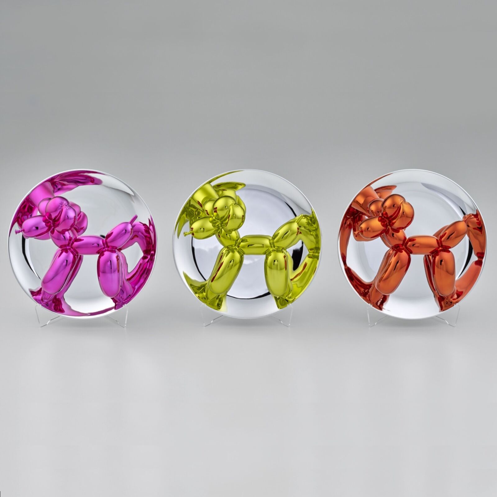 A trio of glossy, metallic balloon-dog sculptures displayed on clear stands against a neutral background.