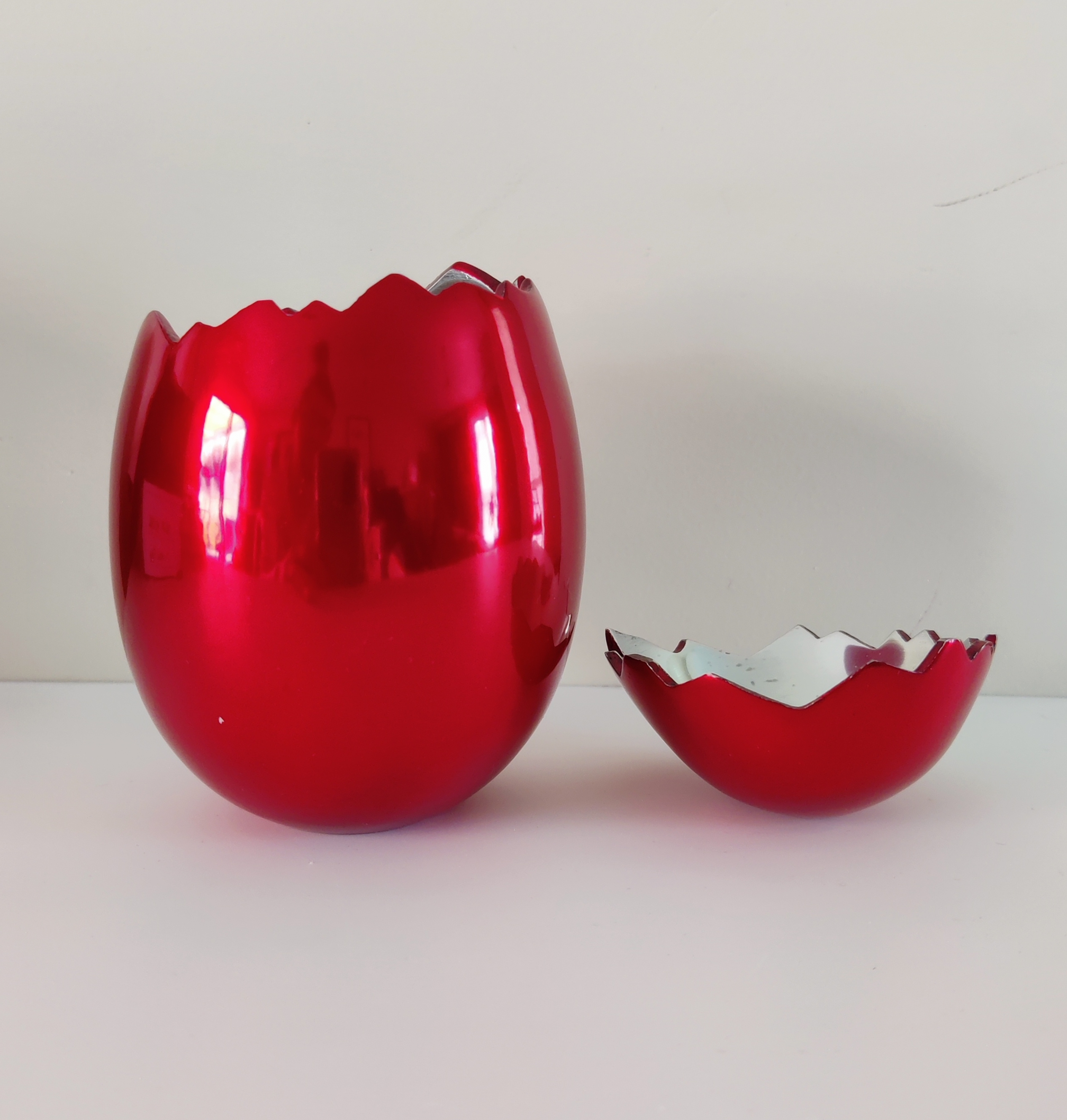 A red vase and a broken glass bowl on a white surface.
