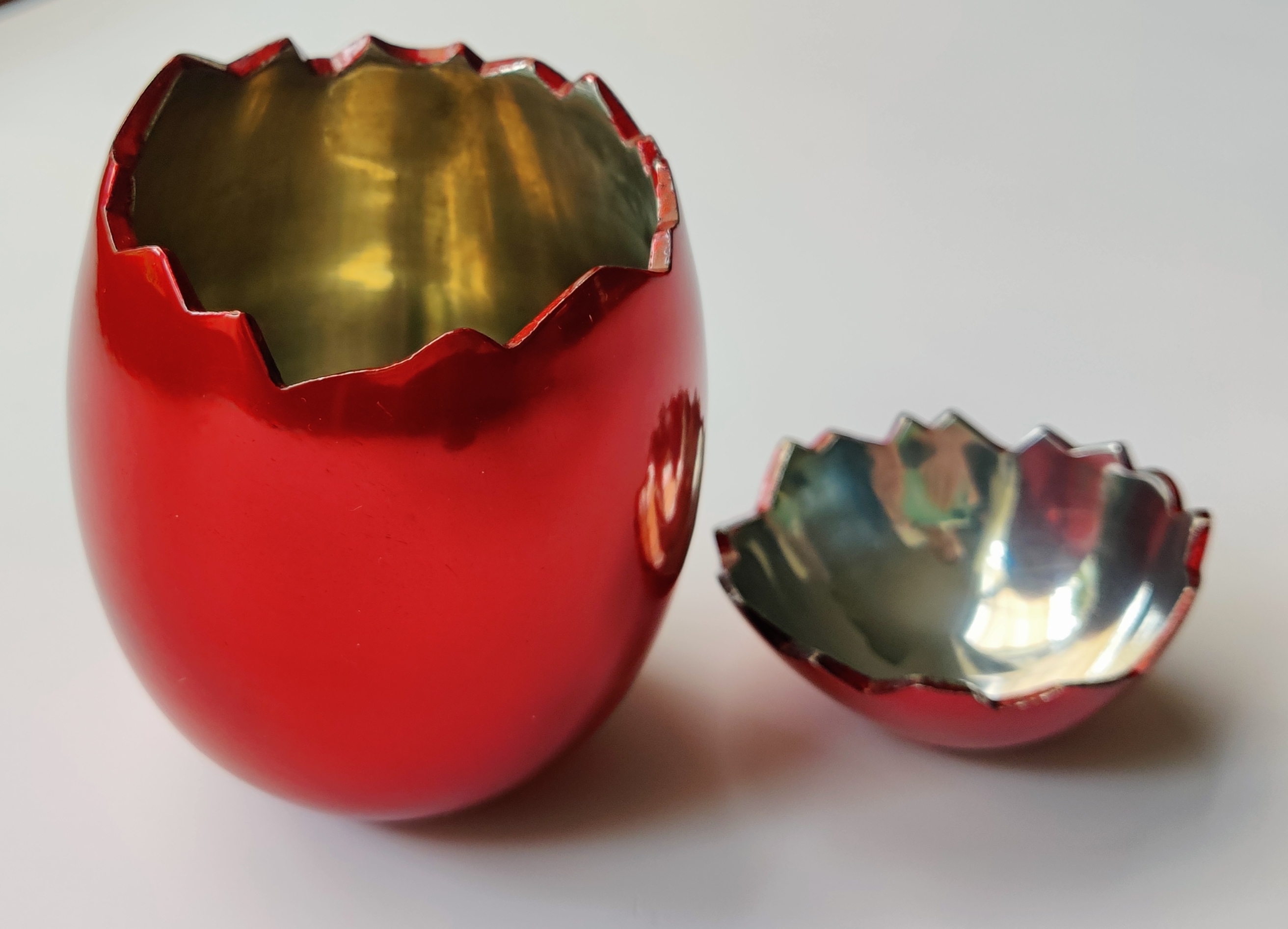 A red vase and a broken glass bowl on a white surface.