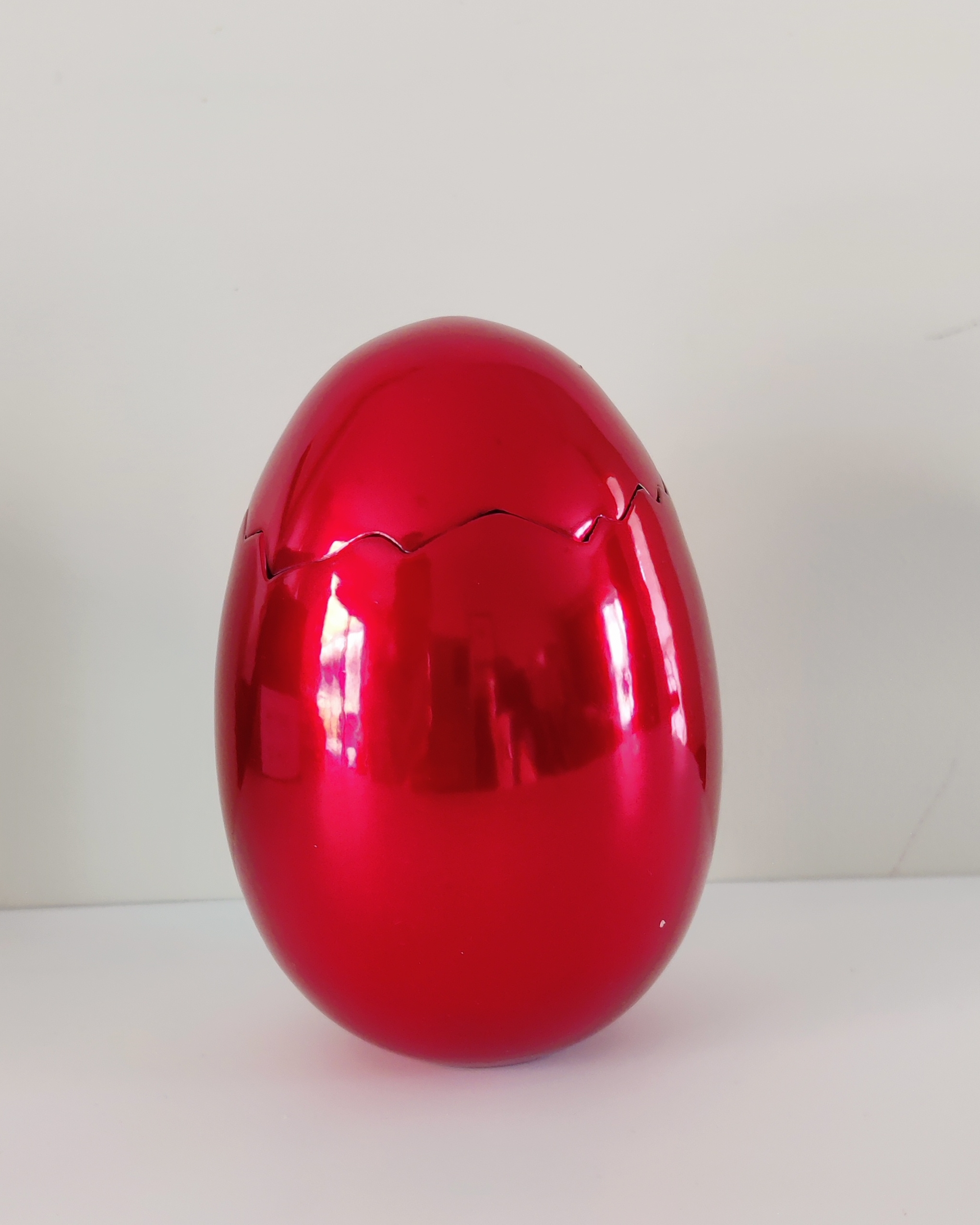 A red vase and a broken glass bowl on a white surface.