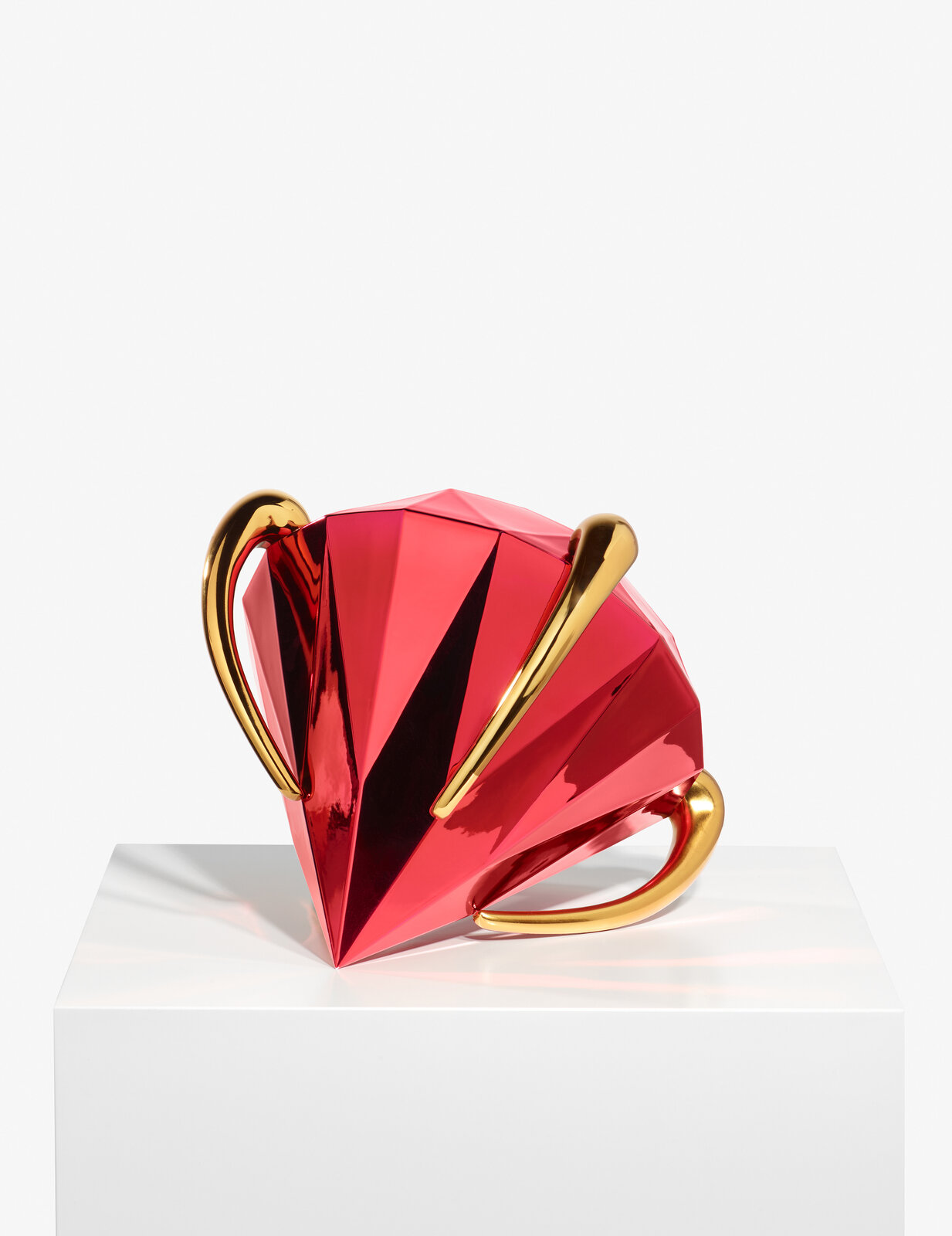 A geometric, faceted pink pitcher with gold handles and feet.