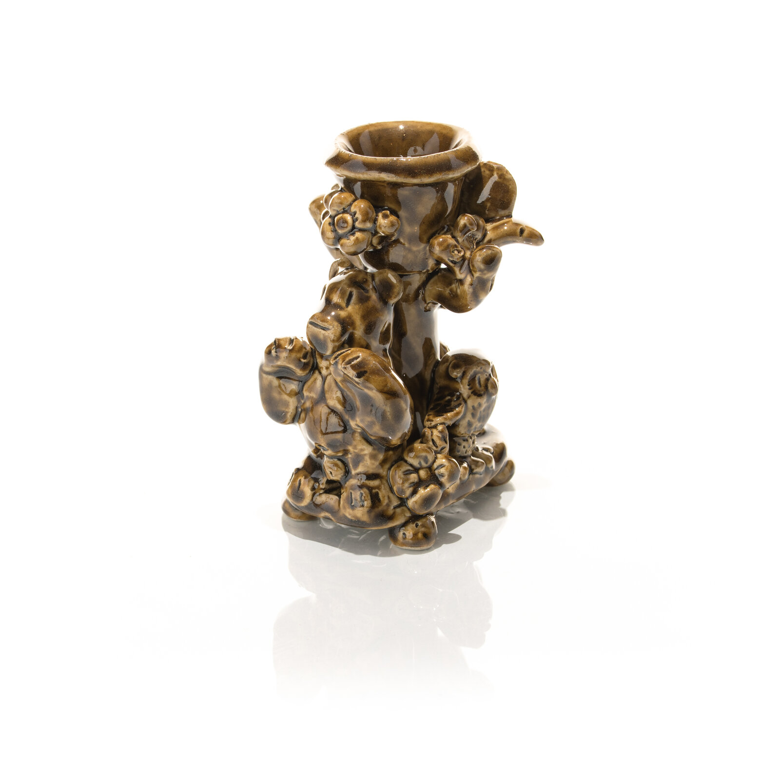 A glossy brown ceramic candlestick featuring a textured, organic design with animal-like figures and floral elements.