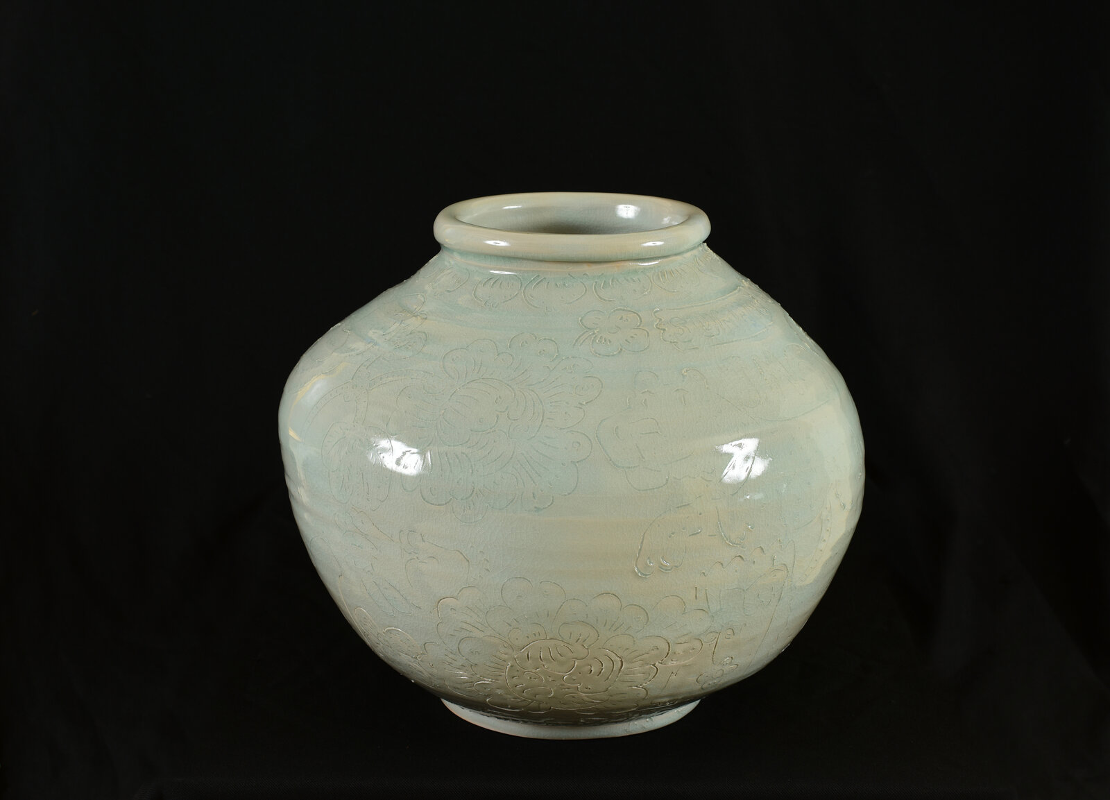 A pale green ceramic jar with embossed floral patterns against a black background.