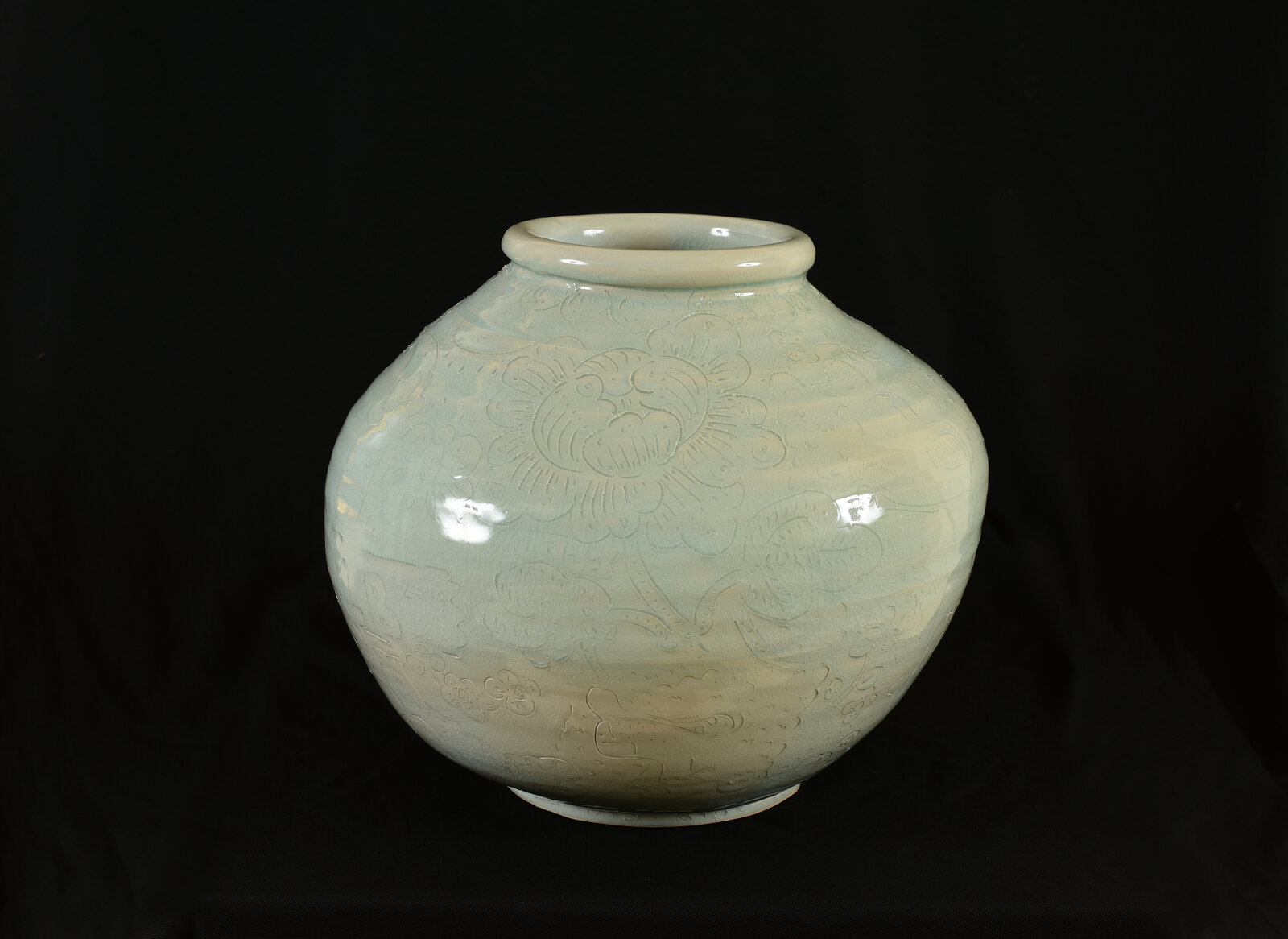 A pale green ceramic jar with embossed floral patterns against a black background.