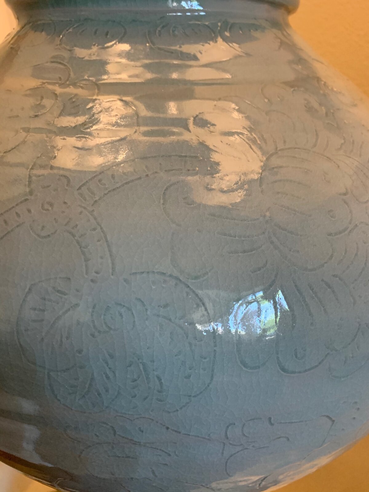 A pale green ceramic jar with embossed floral patterns against a black background.